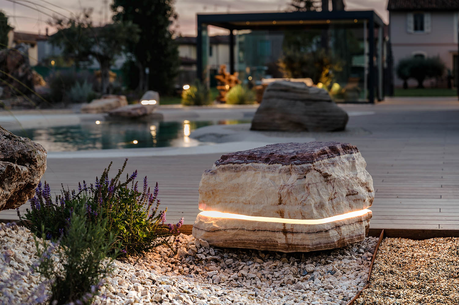 Luminaire sculptural en pierre naturelle illuminant un jardin au crépuscule